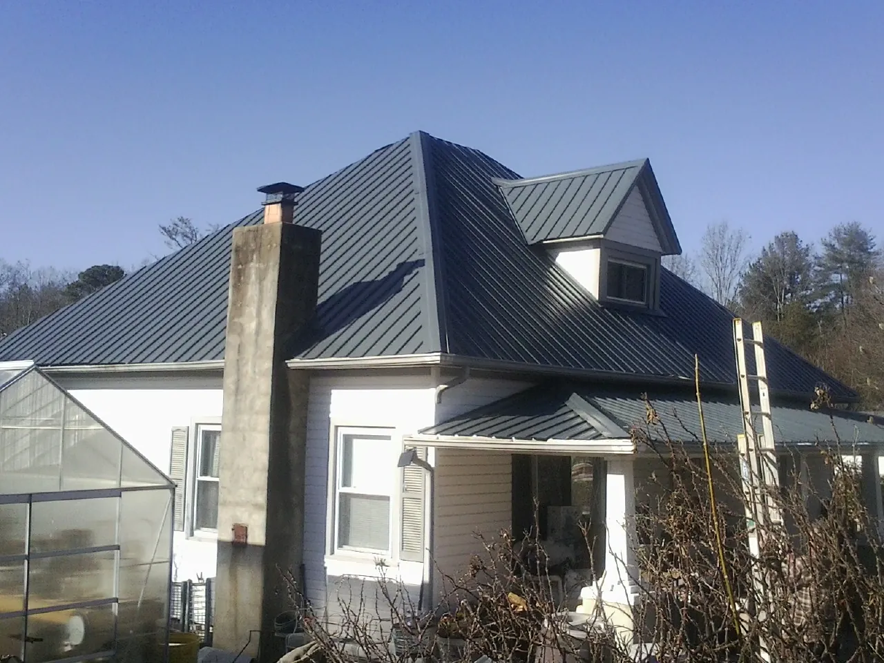 Dark blue standing seam metal roof on a white farmhouse with dormer — Slate & Tile Roof Repair by Roofing Brothers in Mullens