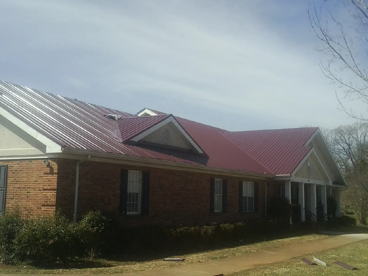 Red metal roof with gabled entries on a long brick building, from a Hail Damage Roof Repair job in Mullens
