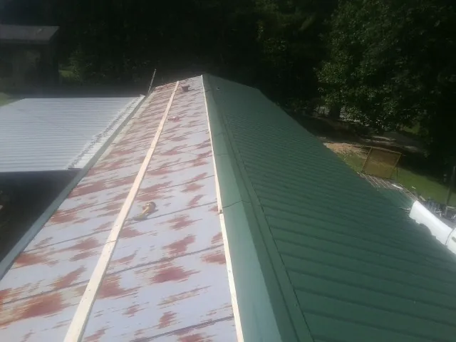 Old rusted panels beside newly installed green metal roofing — Wind Damage Roof Repair by Roofing Brothers in Mullens