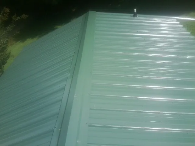 New green metal panels meeting at the ridge of a roof — Flat Roof Repair work by our crew in Mullens