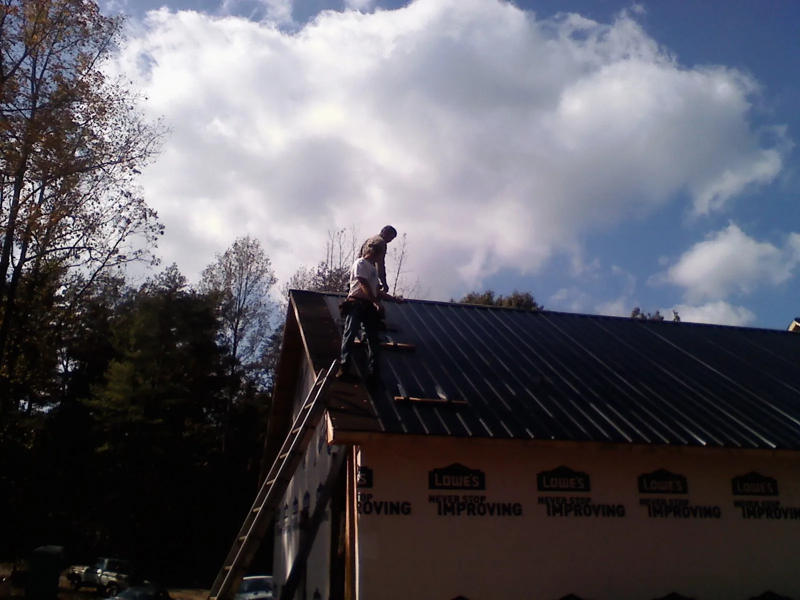 Roofer fastening dark metal panels high against a cloudy sky, from a Roof Inspection job in Mullens