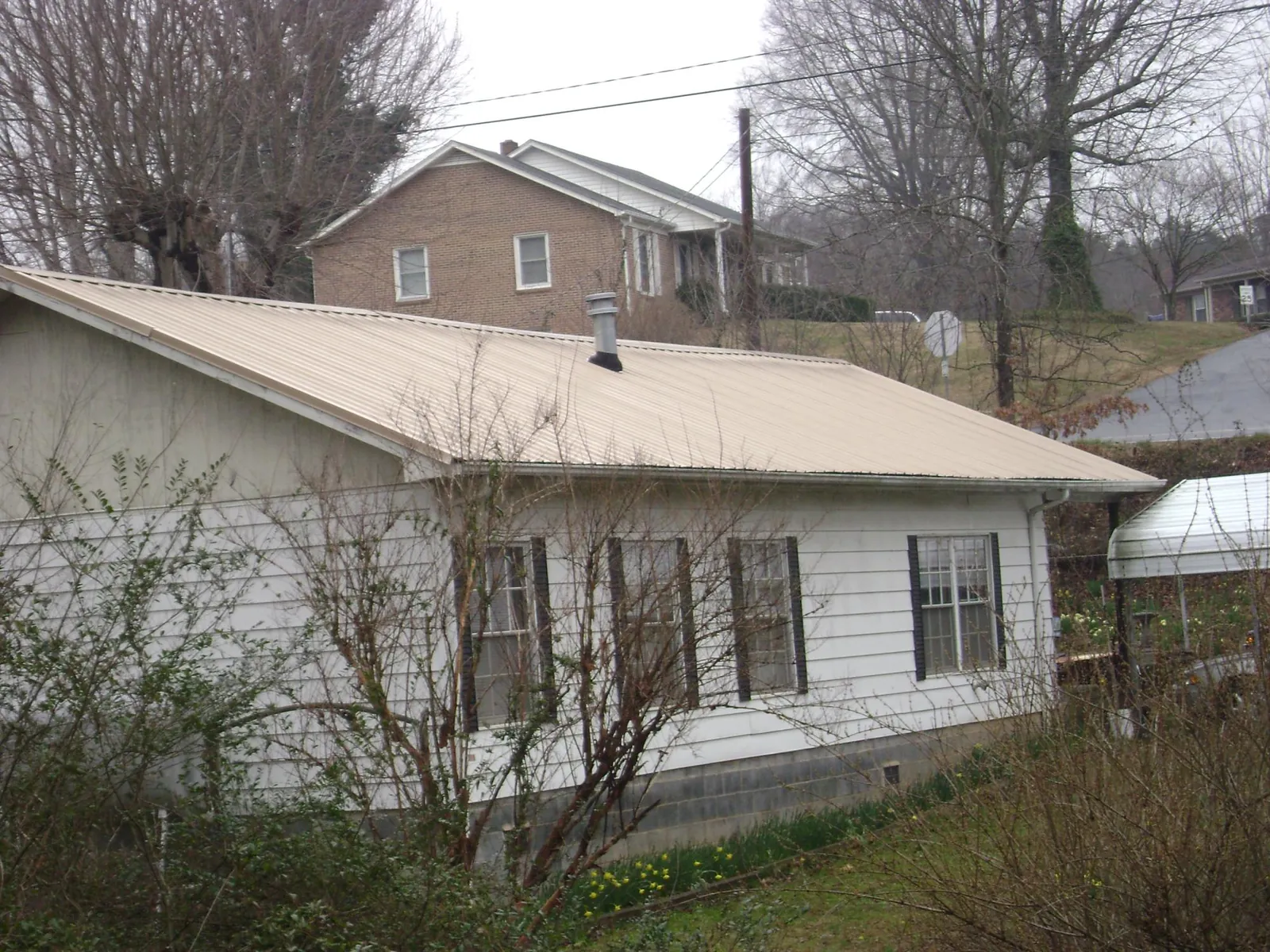 Tan metal roof on a white sided house set into a hillside — Commercial Roofing by Roofing Brothers in Mullens