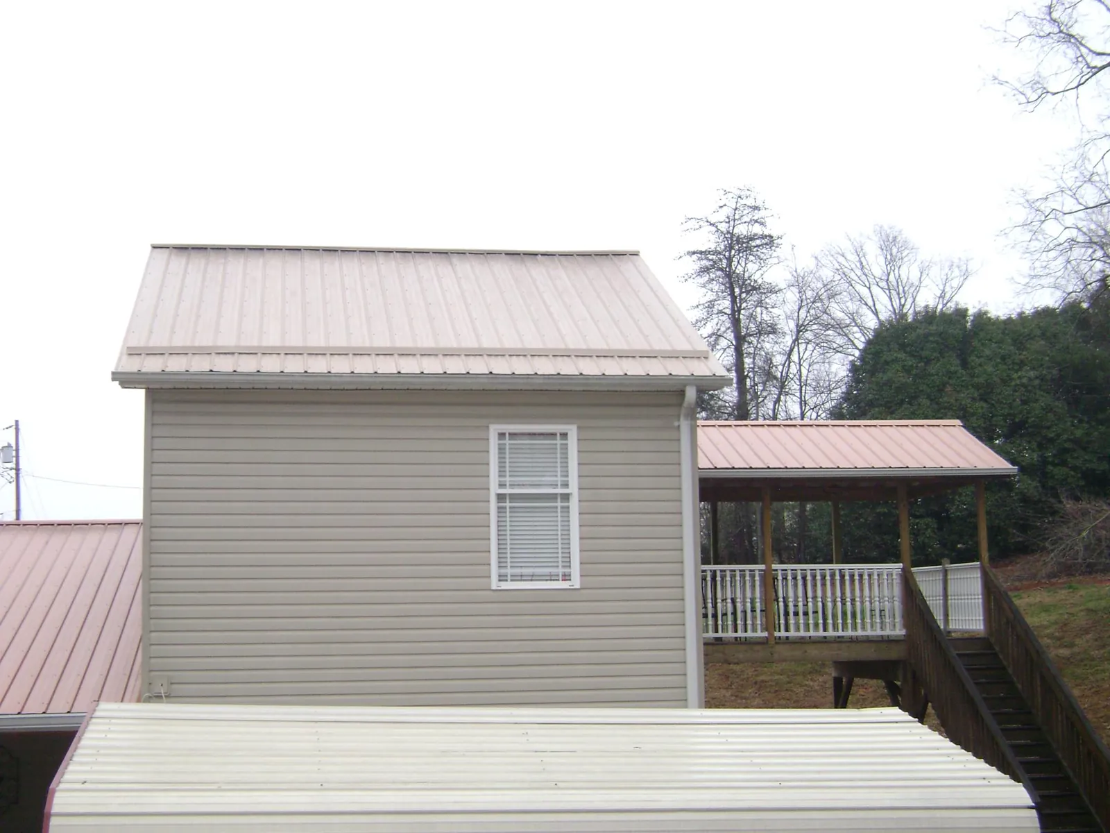 Tan metal roofs on a two story addition and attached porch, from a Roof Replacement job in Mullens